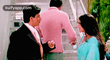 a man in a pink jacket is standing next to a woman in a blue dress and talking to her .