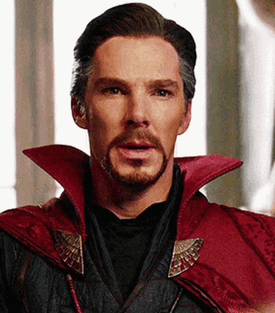 a close up of a man with a beard wearing a red cape and a black shirt .