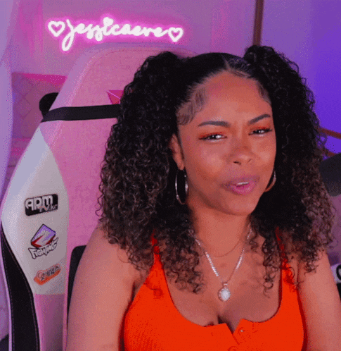 a woman with curly hair is sitting in front of a neon sign that says jessleaere
