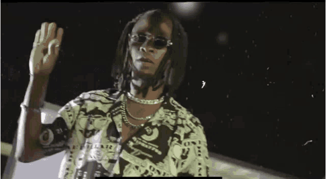 a man with dreadlocks wearing sunglasses and a necklace is standing in the dark .
