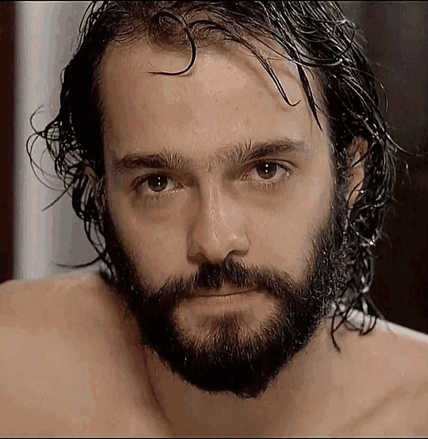 a shirtless man with a beard and wet hair looks at the camera