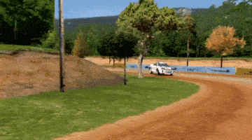 a white car is driving down a dirt road with a blue banner that says ' hot wheels ' on it