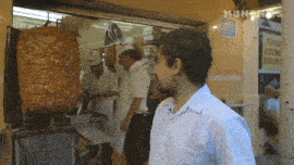 a man in a blue shirt is standing in front of a kebab stand