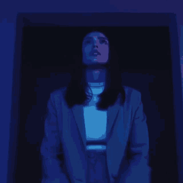 a woman in a suit is standing in a dark room with blue lights behind her .