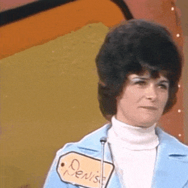 a woman wearing a blue jacket and white turtleneck has a tag that says denise on it