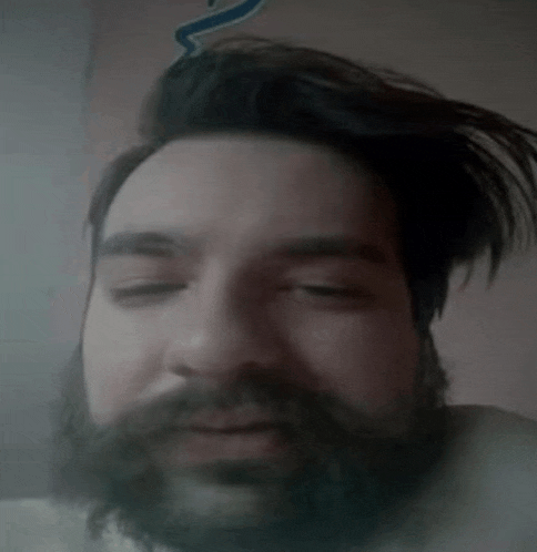 a man with a beard and long hair is making a funny face with his eyes closed .