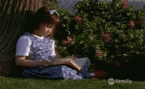 a little girl is sitting under a tree reading a book on abc family