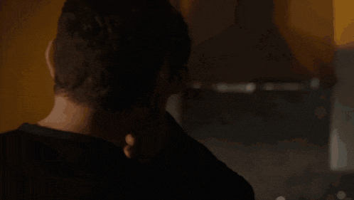 a man in a black shirt is standing in a dark room looking at something .