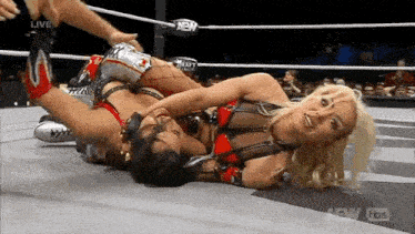 two women are wrestling in a wrestling ring and one of them is laying on the floor .
