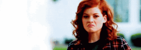 a woman with red hair is wearing a plaid shirt and making an angry face .