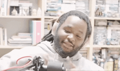 a man with dreadlocks is wearing headphones and smiling in front of a bookcase .