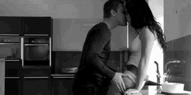 a man and woman are kissing in a kitchen in a black and white photo .