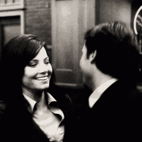a black and white photo of a man and woman looking at each other .