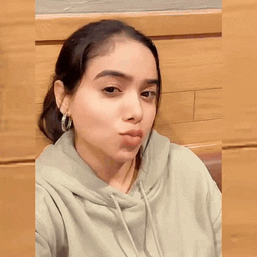a woman wearing a grey hoodie and hoop earrings is making a funny face