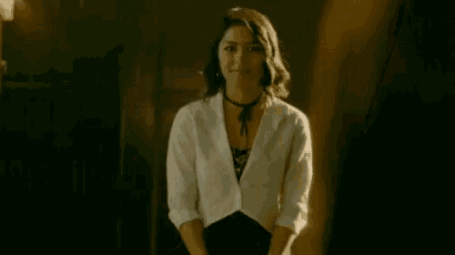 a woman in a white shirt and black skirt is standing in a dark room and smiling .