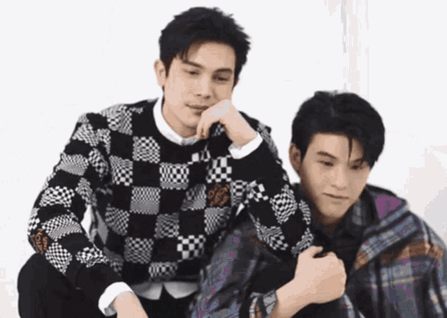 two young men are sitting next to each other and one is wearing a checkered sweater