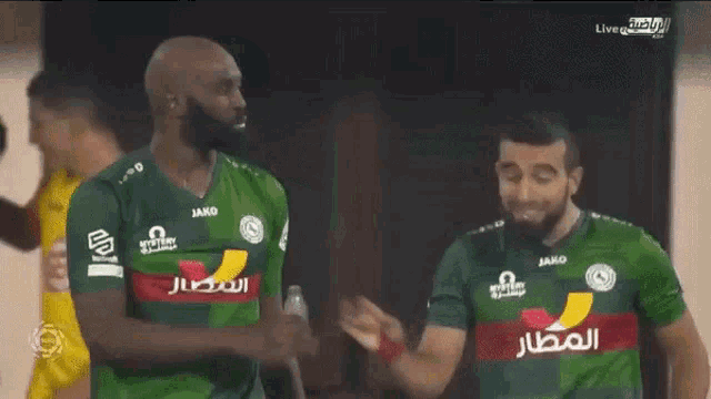 two soccer players wearing green jerseys with jako on the front