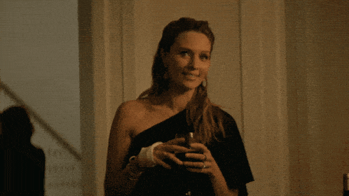 a woman in a black dress is holding a glass of wine and smiling