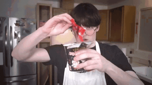a man wearing glasses and an apron is eating a cup of food