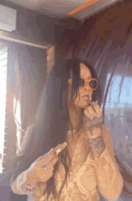 a woman wearing sunglasses is applying lip gloss to her lips .