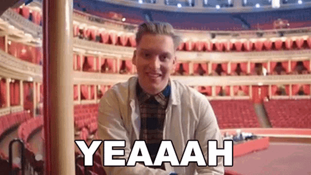 a man is sitting in a stadium with the words yeaaah written on the screen .