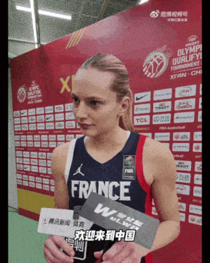 a woman in a france jersey holds a microphone in front of a wall of sponsors