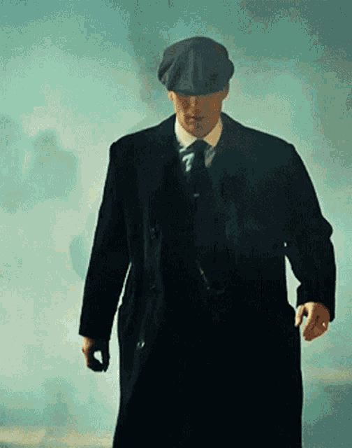 a man in a suit and hat is walking through a foggy area .