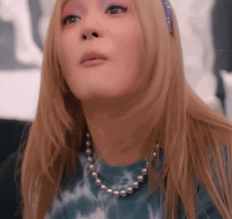 a woman wearing a blue tie dye shirt and a pearl necklace looks up