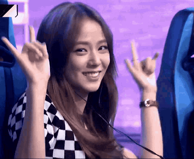 a woman wearing headphones is sitting in a blue chair and making a devil horns sign with her hands .