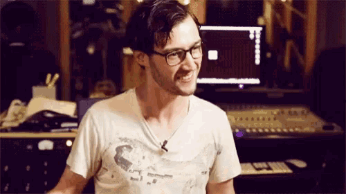 a man wearing glasses and a white shirt is smiling in front of a computer screen
