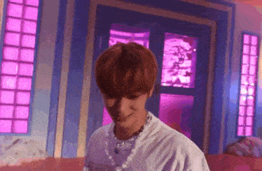 a young man with red hair and a pearl necklace is standing in front of a pink door .