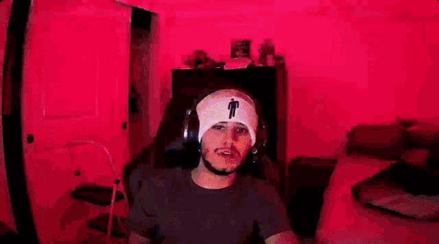 a man wearing a billie eilish beanie is sitting in a chair with headphones on .