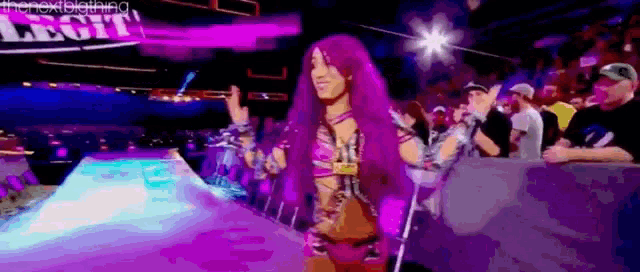 a woman with purple hair is standing in front of a crowd in a wrestling ring .