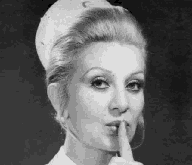 a woman in a nurse 's uniform is holding her finger to her mouth .