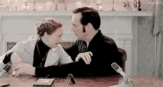a man and woman are sitting at a table with a microphone .