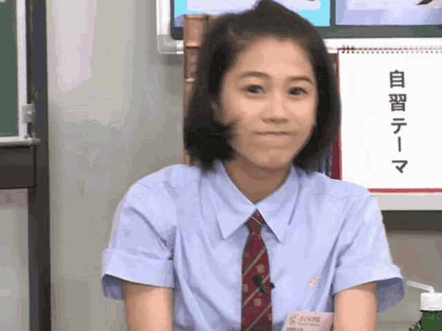 a girl in a blue shirt and red tie is smiling in front of a sign with chinese writing