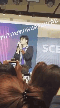 a man is singing into a microphone in front of a banner that says sce