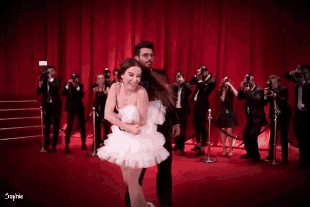 a man is carrying a woman in a white dress on a red carpet
