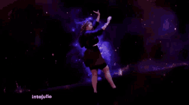 a woman is dancing in front of a galaxy and the words intojulio are visible on the bottom