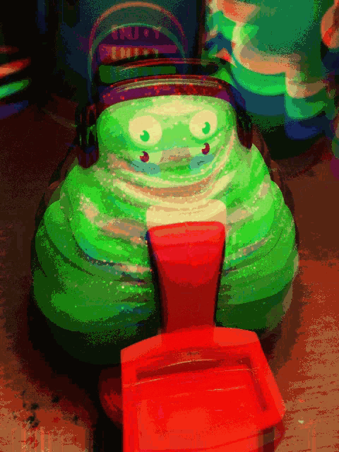 a green toy with headphones on is sitting on a red container
