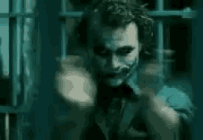 the joker is holding a gun in his hand and pointing it at someone .