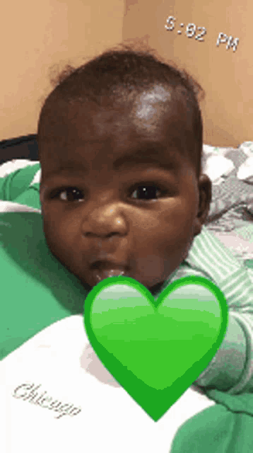 a baby is laying on a bed with a green heart in front of his mouth