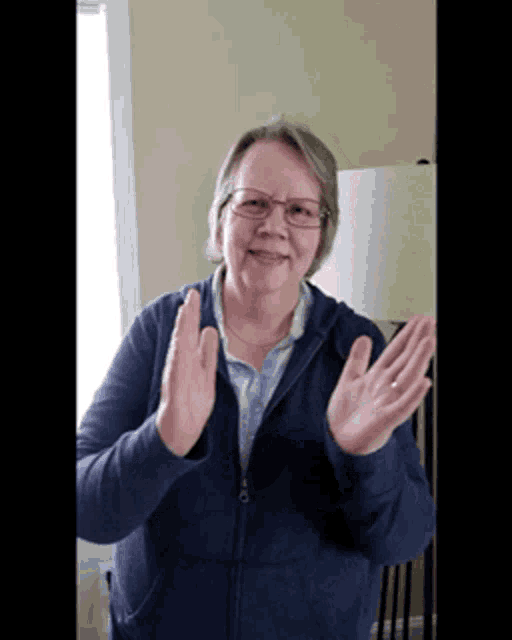 an older woman wearing glasses and a blue jacket is clapping her hands
