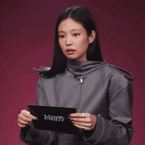 a woman in a grey jacket holds a variety magazine