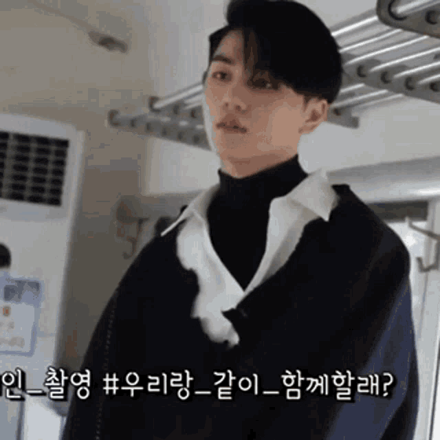a young man wearing a black turtleneck and a white shirt is standing in front of a clothes drying rack ..