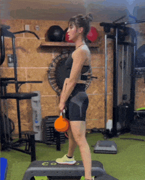 a woman is lifting a kettlebell in a gym with a sign that says exit