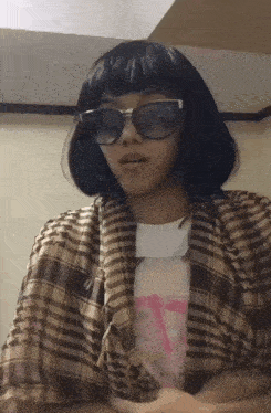 a woman wearing sunglasses and a plaid shirt has a wig on
