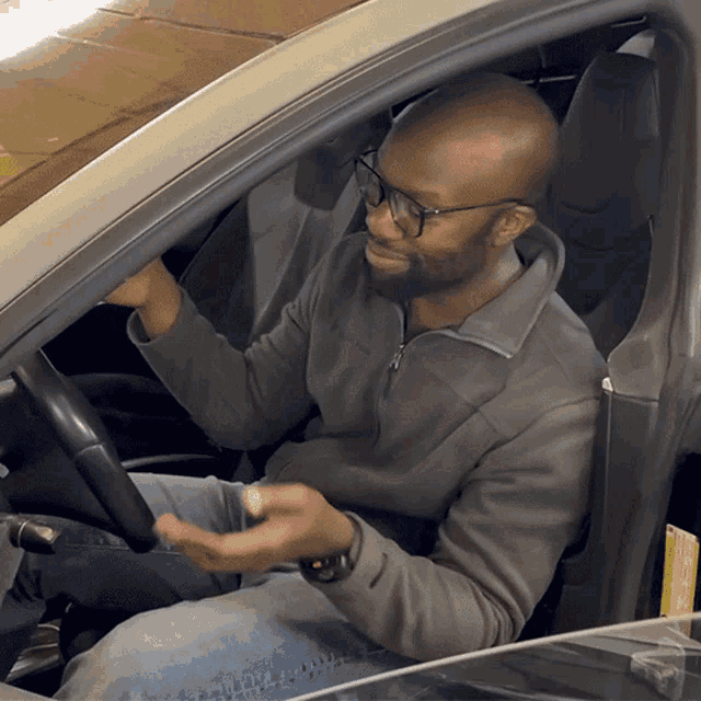 a man wearing glasses sits in a car