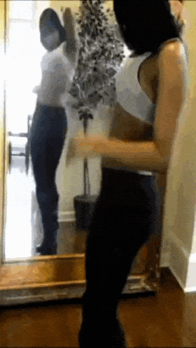 a woman is dancing in front of a mirror with a plant in the background