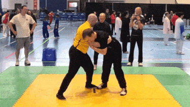 a man in a yellow shirt is wrestling another man in black pants